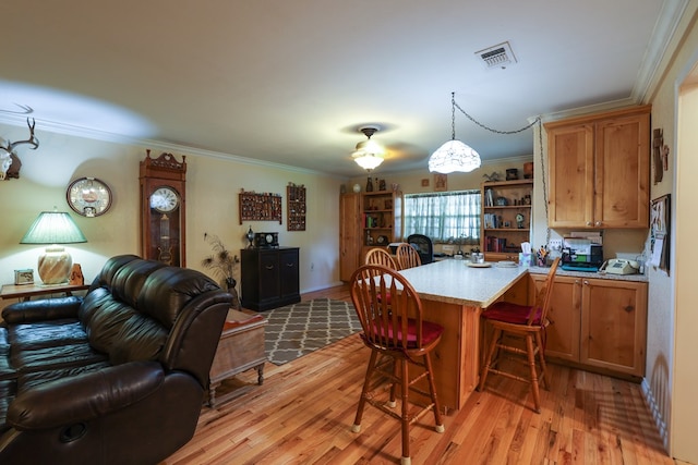 kitchen with hanging light fixtures, crown molding, light wood-type flooring, and a kitchen bar