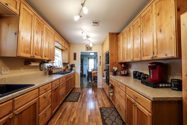 kitchen featuring sink, rail lighting, light hardwood / wood-style floors, black appliances, and light stone countertops