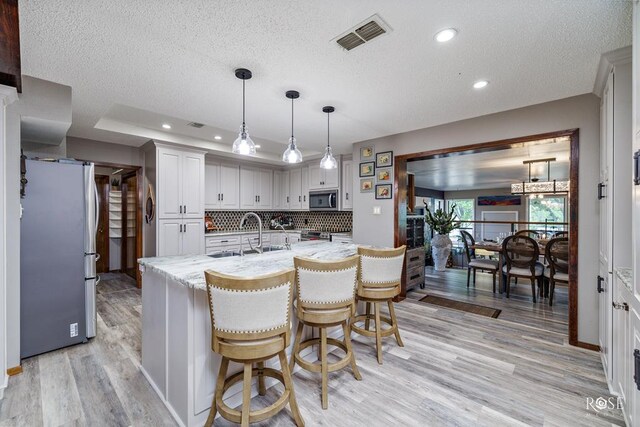 kitchen featuring sink, white cabinetry, stainless steel appliances, light stone counters, and decorative light fixtures