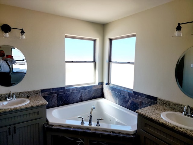 full bath featuring a jetted tub, two vanities, and a sink