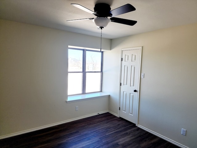 spare room with dark wood-style flooring, a healthy amount of sunlight, ceiling fan, and baseboards