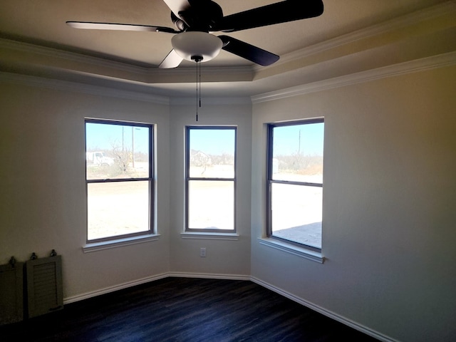 spare room with a tray ceiling, crown molding, dark wood finished floors, ceiling fan, and baseboards