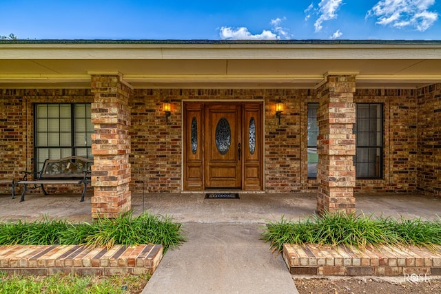 doorway to property with a porch and brick siding