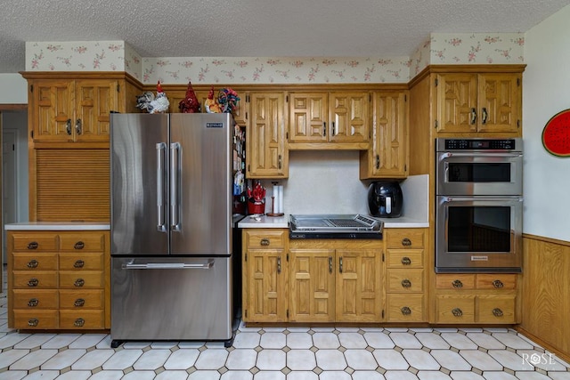 kitchen with appliances with stainless steel finishes, wainscoting, light countertops, and brown cabinets