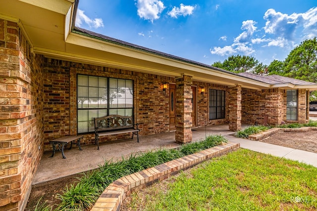 view of exterior entry with a porch and brick siding