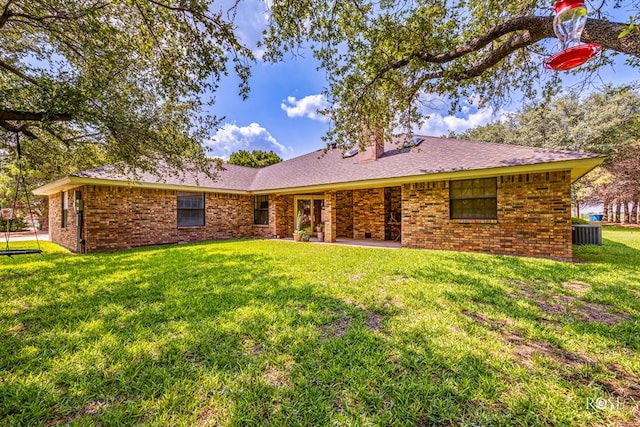 rear view of house with cooling unit, brick siding, and a yard