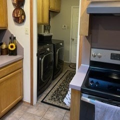 kitchen featuring stainless steel range with electric stovetop, separate washer and dryer, wall chimney exhaust hood, and light tile patterned flooring