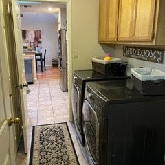 clothes washing area with cabinets, washing machine and dryer, and light tile patterned floors