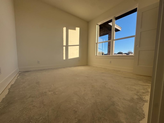 spare room featuring unfinished concrete floors, baseboards, and vaulted ceiling