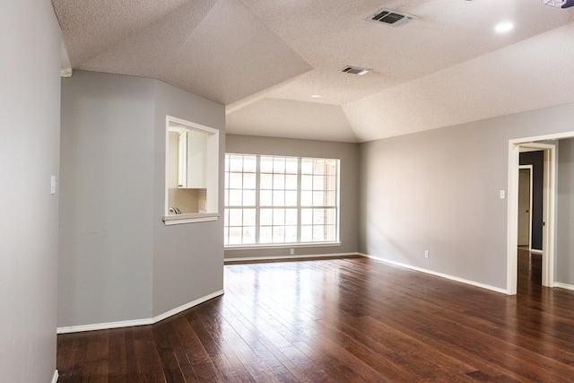 spare room with dark wood-style floors, lofted ceiling, visible vents, and baseboards
