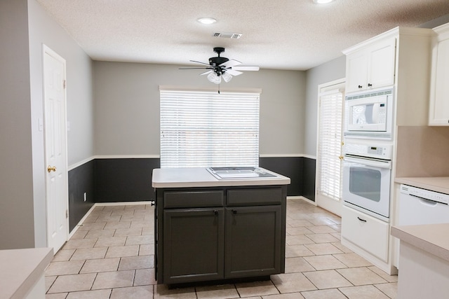 kitchen featuring white appliances, a kitchen island, visible vents, white cabinetry, and light countertops