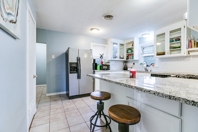 kitchen featuring light stone counters, white cabinetry, a kitchen breakfast bar, and stainless steel fridge with ice dispenser