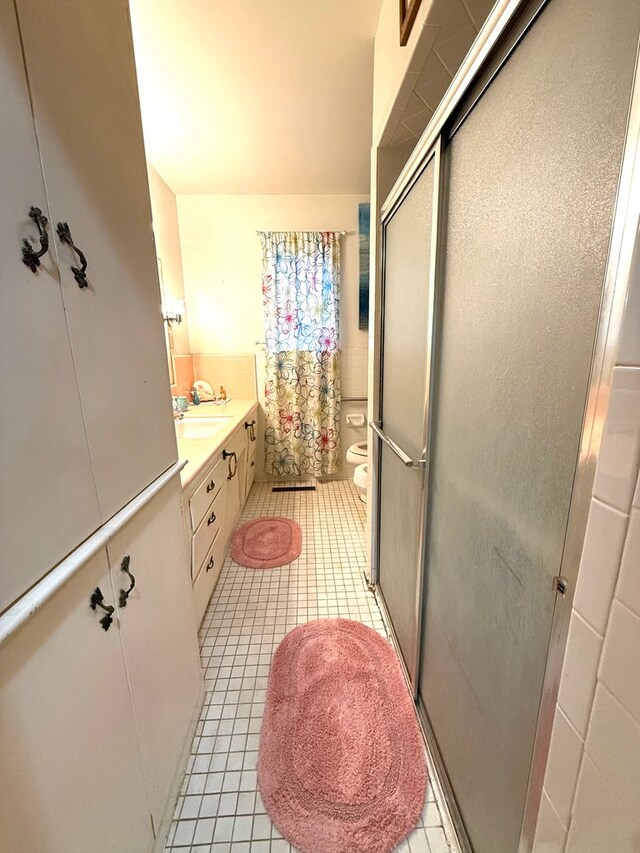 bathroom featuring tile patterned floors, toilet, a shower with shower door, a bidet, and vanity