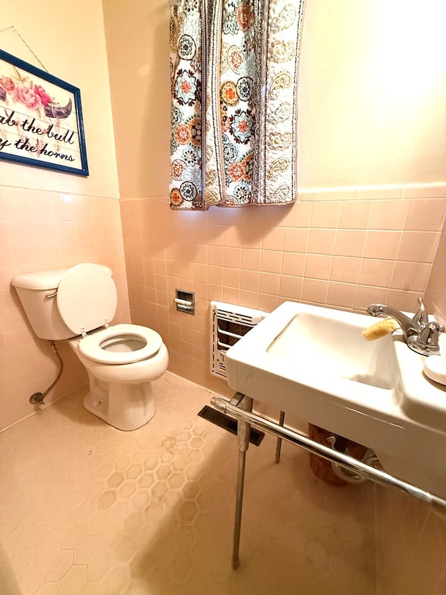 bathroom with tile patterned floors, toilet, sink, heating unit, and tile walls