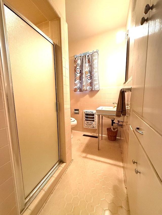 bathroom with heating unit, a shower with shower door, tile walls, tile patterned flooring, and toilet