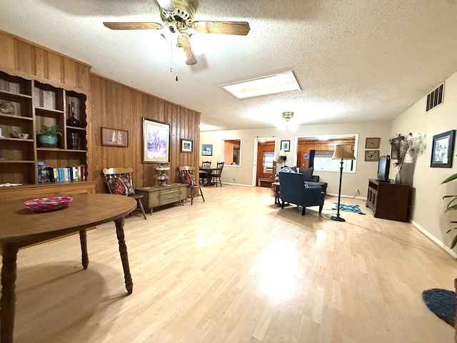 home office featuring ceiling fan, wooden walls, light hardwood / wood-style floors, and a textured ceiling