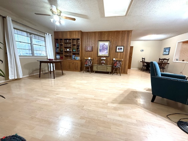 interior space with ceiling fan, light wood-type flooring, a textured ceiling, and wood walls