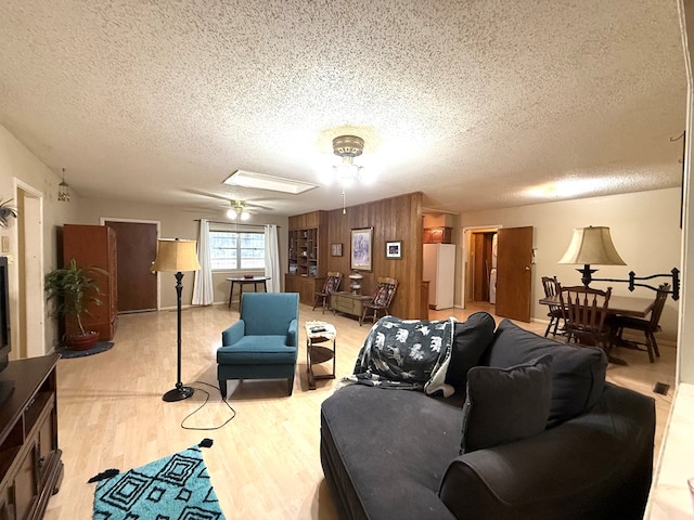 living room with a textured ceiling, wooden walls, ceiling fan, and light wood-type flooring