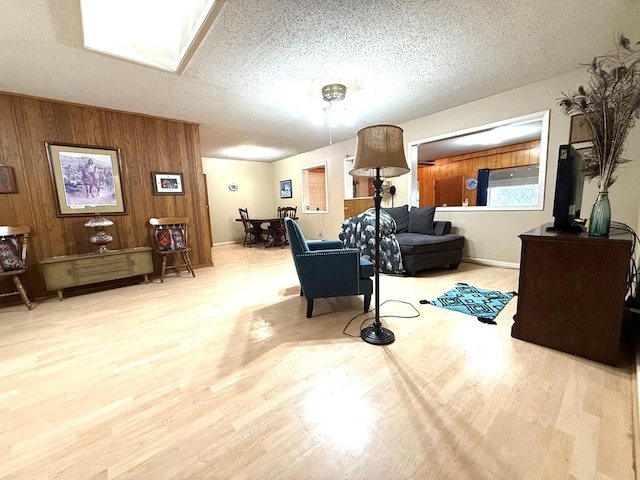 living room with wooden walls, a textured ceiling, and light wood-type flooring