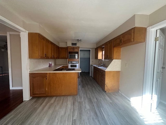 kitchen with sink, gas stovetop, kitchen peninsula, light hardwood / wood-style floors, and white oven