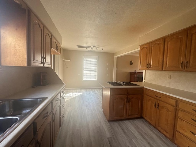 kitchen featuring stainless steel gas stovetop, sink, light hardwood / wood-style floors, kitchen peninsula, and a textured ceiling