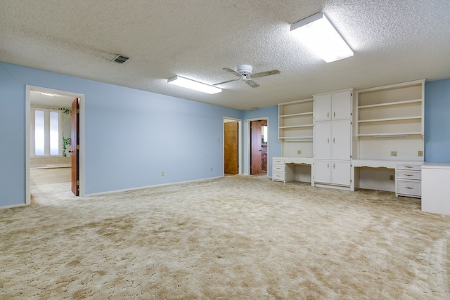 unfurnished bedroom with ceiling fan, built in desk, light carpet, and a textured ceiling