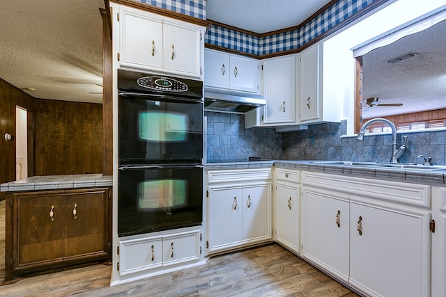 kitchen with sink, white cabinetry, double oven, tile counters, and a textured ceiling