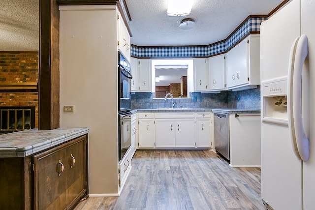 kitchen featuring sink, a textured ceiling, stainless steel dishwasher, white refrigerator with ice dispenser, and white cabinets