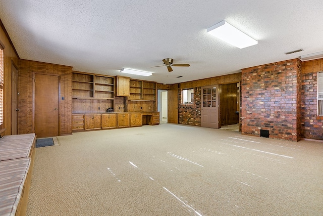 unfurnished living room with ceiling fan, carpet flooring, a textured ceiling, and wood walls