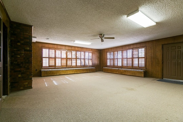 empty room featuring a textured ceiling, carpet, ceiling fan, and wood walls