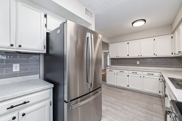 kitchen with white cabinets, stainless steel fridge, a textured ceiling, and decorative backsplash