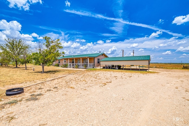 view of front of house with a detached carport, a porch, dirt driveway, and metal roof