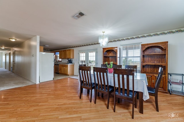 dining space featuring light wood-style flooring, french doors, visible vents, and a chandelier