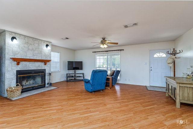 living room with ceiling fan, visible vents, a stone fireplace, and light wood-style flooring