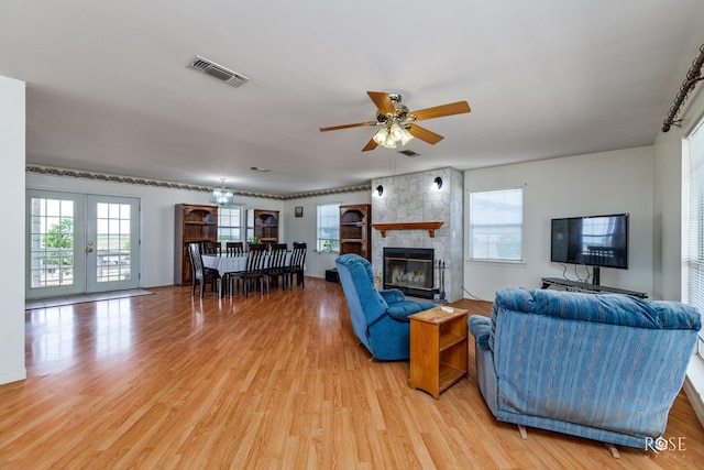 living room featuring visible vents, light wood-style flooring, french doors, a fireplace, and ceiling fan