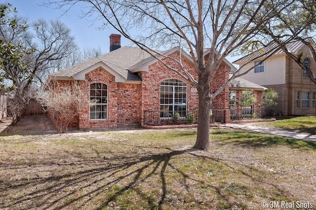 view of front of home with fence, roof with shingles, a front yard, brick siding, and a chimney