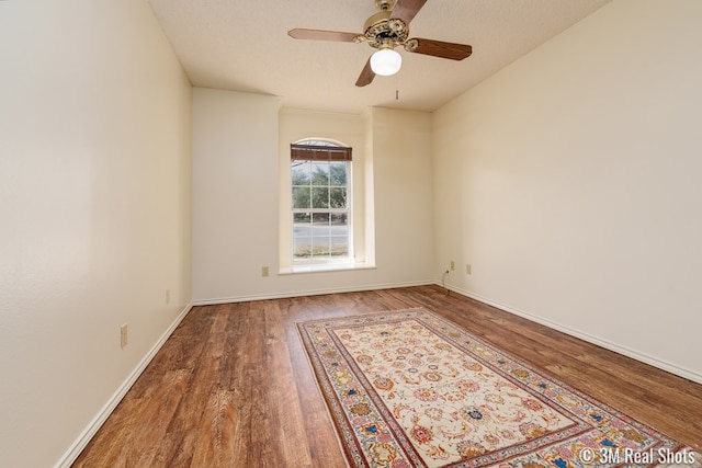 empty room featuring a textured ceiling, a ceiling fan, baseboards, and wood finished floors