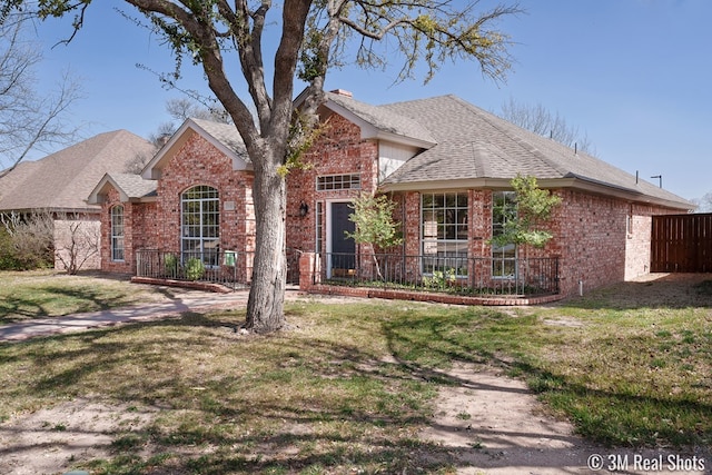 view of front of property featuring brick siding, a shingled roof, a front lawn, and fence