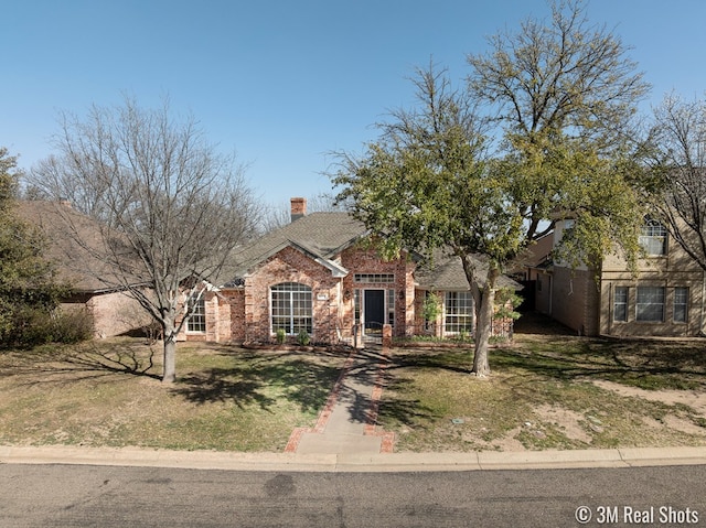 view of front facade with brick siding, a chimney, and a front yard