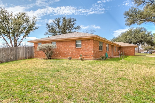 view of side of property featuring brick siding, a yard, and fence