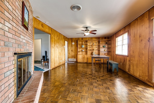 unfurnished living room with ceiling fan, wood walls, a brick fireplace, and visible vents