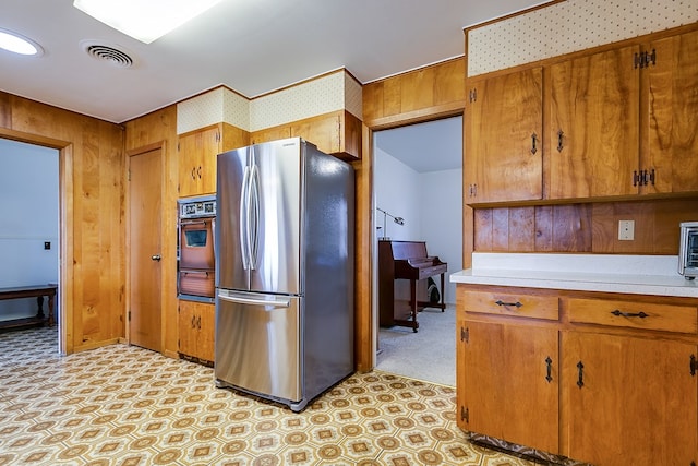 kitchen with light countertops, visible vents, wall oven, freestanding refrigerator, and brown cabinetry