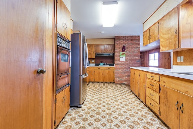 kitchen featuring brown cabinets, freestanding refrigerator, oven, light countertops, and light floors