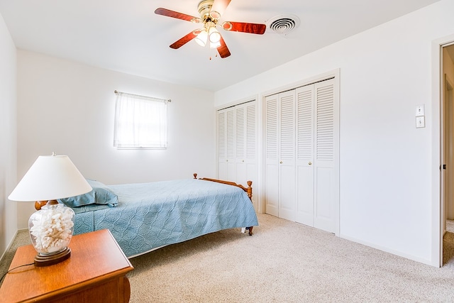 carpeted bedroom with a ceiling fan, visible vents, baseboards, and two closets