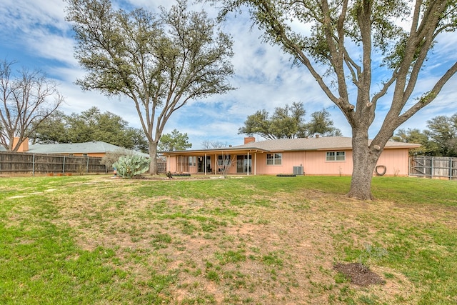 rear view of property featuring a yard, central AC unit, a chimney, and fence