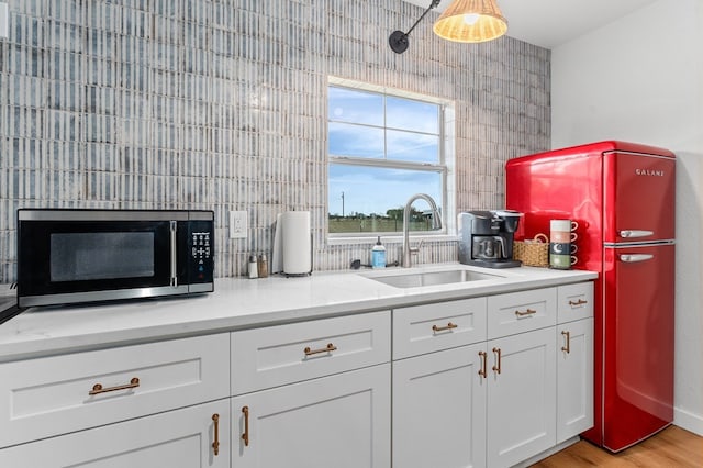 kitchen with sink, refrigerator, light stone counters, white cabinets, and light wood-type flooring