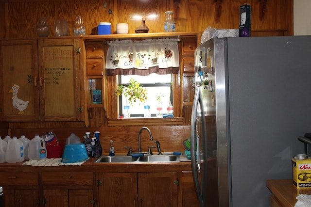 kitchen with sink, stainless steel fridge, and wood walls