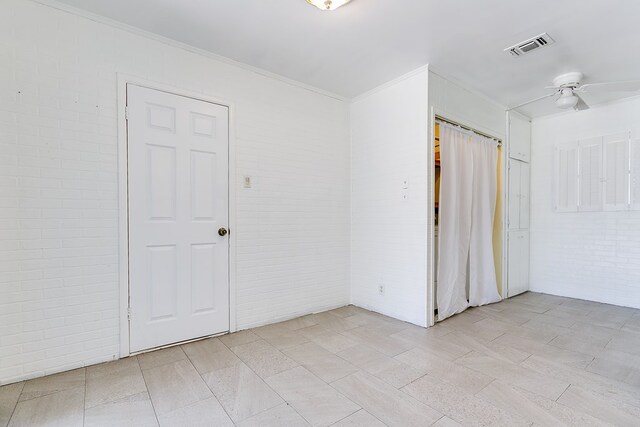 unfurnished room featuring ornamental molding, ceiling fan, and brick wall