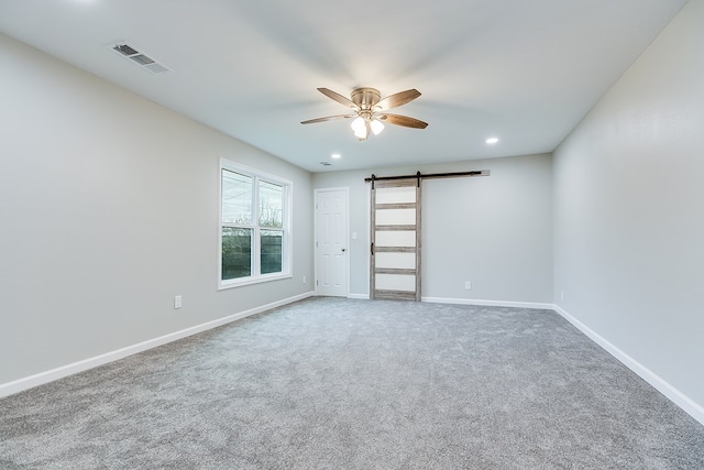 empty room featuring ceiling fan, a barn door, and carpet