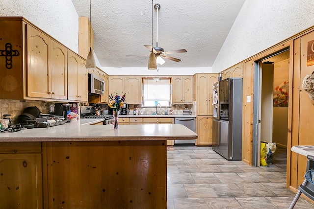 kitchen with a peninsula, ceiling fan, a sink, stainless steel appliances, and tasteful backsplash